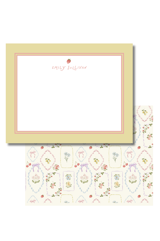 A stationery set featuring a personalized note card and matching patterned envelope. The card has a pale yellow border, a thin pink inner border, and a blank white writing area with the name 'Emily Sullivan' and a small strawberry printed at the top.